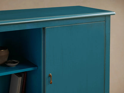 Varzi Cabinet in teal with hand-painted details. Features an antique finish, pendant pull hardware, and open shelf with books and bowl.