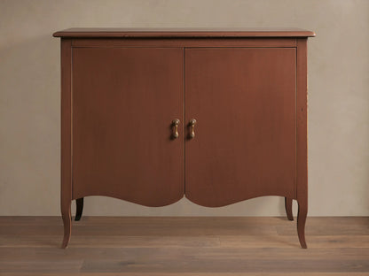 Varzi Cabinet made of warm brown wood with two doors, ornate pendant pull handles, and curved legs on a wood floor.