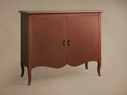 Varzi Cabinet made of warm brown wood with two doors, ornate pendant pull handles, and curved legs on a wood floor.