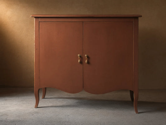 Varzi Cabinet made of warm brown wood with two doors, ornate pendant pull handles, and curved legs on a wood floor.
