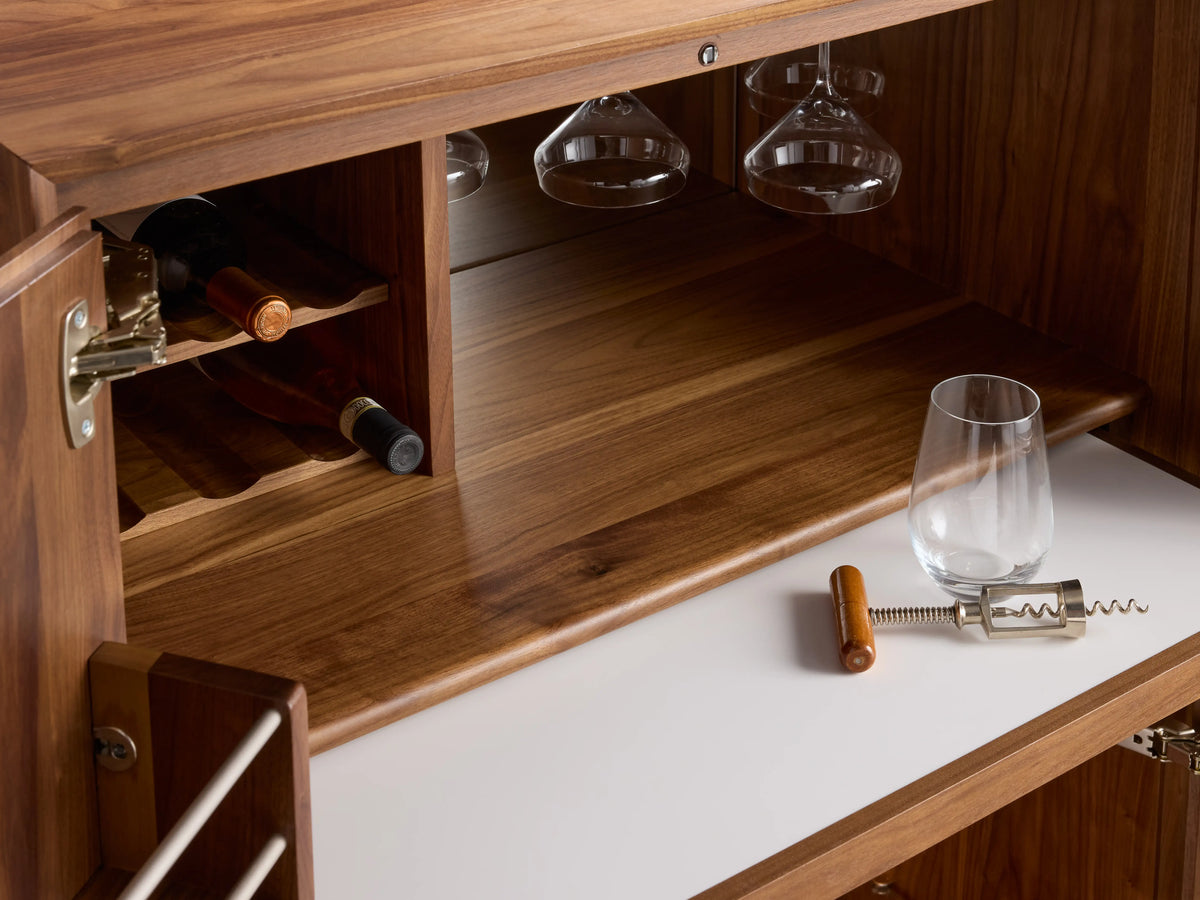 Willard Bar Cabinet open, showing walnut wood finish, brass hardware, stemware rack, shelves with bottles and glasses, and pull-out tray.