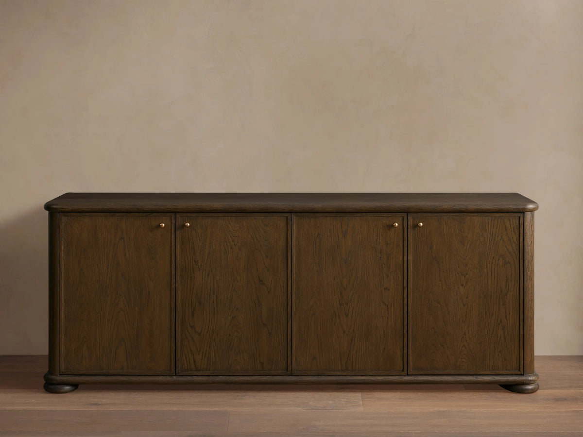 Warby Sideboard made from solid oak wood with a rich mocha finish. Features four cabinet doors with brass hardware on a smooth wood floor.