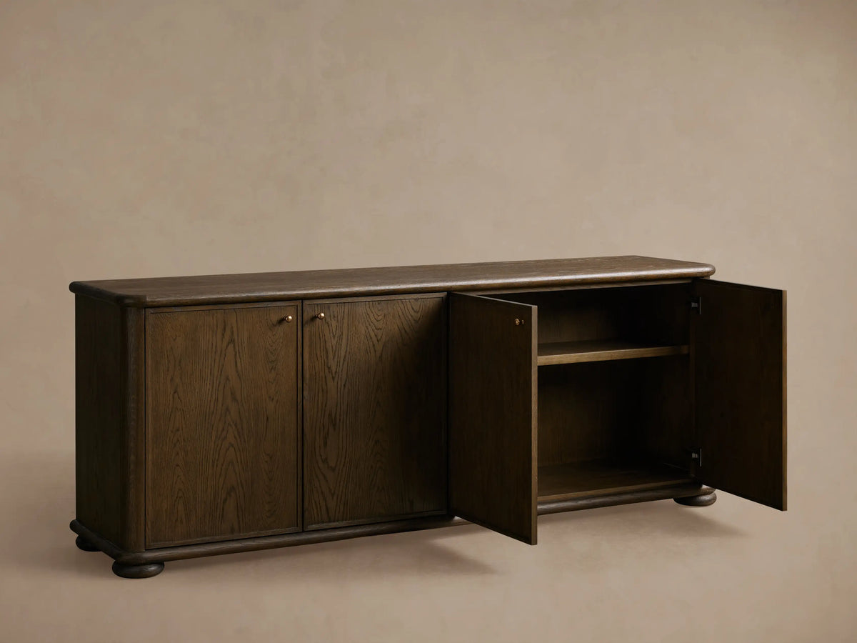 Warby Sideboard made from solid oak wood with a rich mocha finish. Features four cabinet doors with brass hardware on a smooth wood floor.