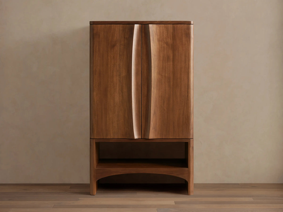 Westyn Bar Cabinet, medium brown wood, two doors with curved vertical finger pulls, and an open lower shelf.