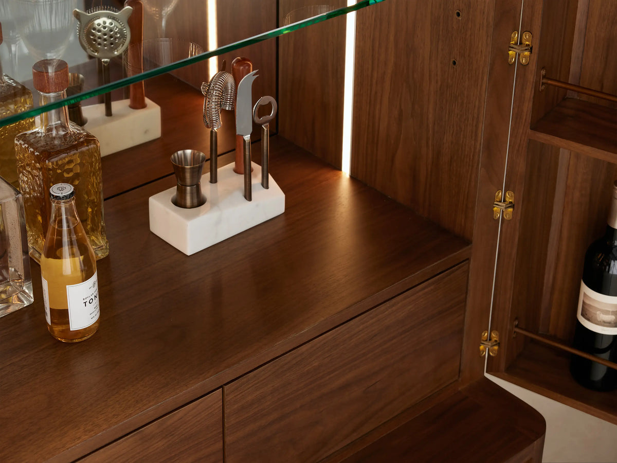 Westyn Bar Cabinet, open. Dark wood cabinet with doors revealing mirrored interior with LED, glass shelf, brass rack, drawers.