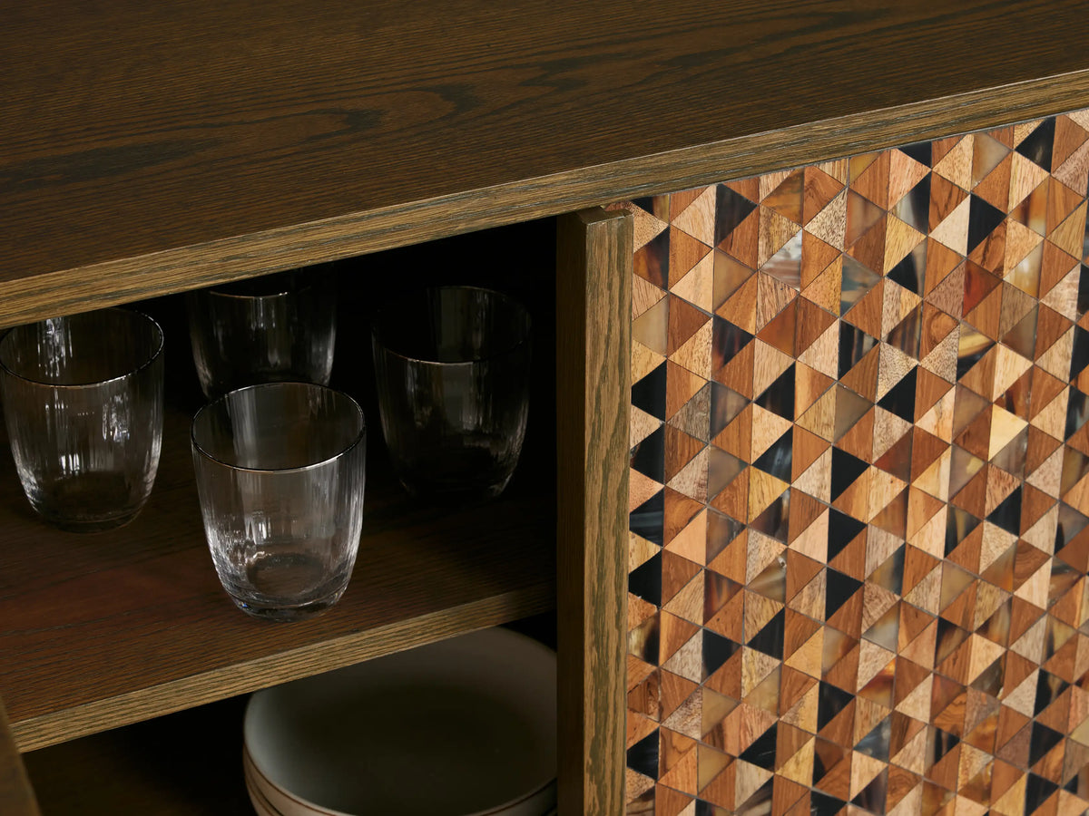 Zansi Sideboard with dark oval top & base. Doors feature an intricate mosaic of triangular wood & horn pieces. One door is ajar, revealing shelves.