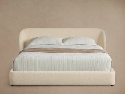 Adalynn Bed: Cream boucle upholstered bed with curved headboard, light striped bedding, and a taupe throw on wood floor.