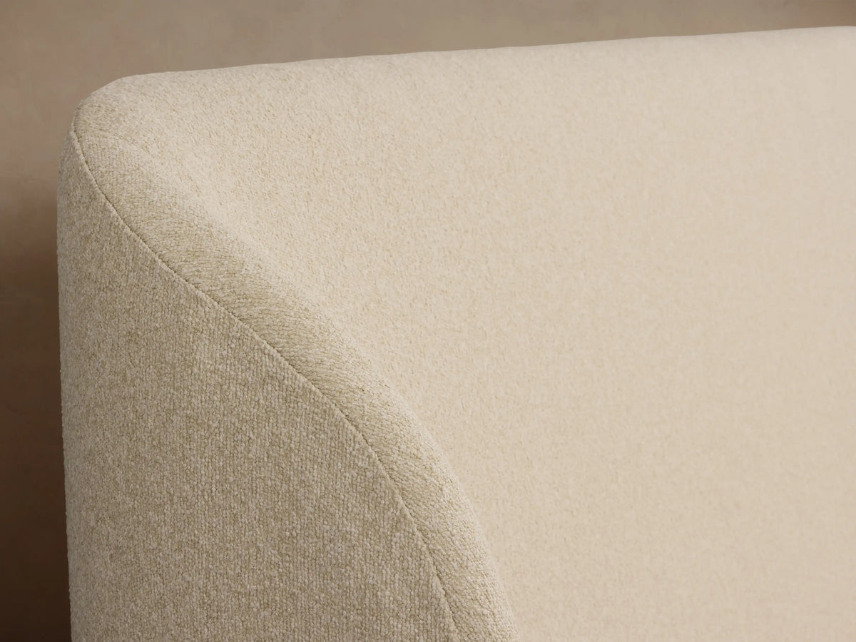 Adalynn Bed, centered, upholstered in textured cream fabric with rounded headboard. Features light striped bedding & brown throw.