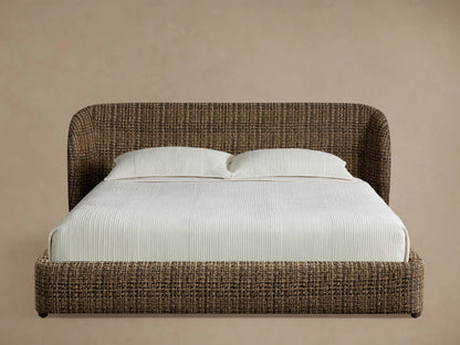 Adalynn Bed with a brown & black tweed-like upholstered, curved headboard & low frame, dressed with white bedding & pillows, on wood floor.