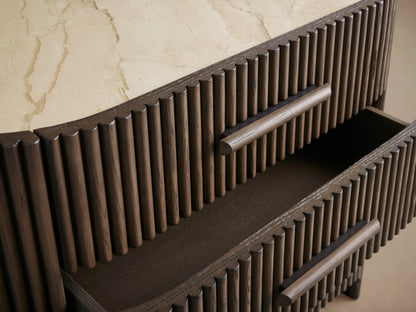 Astor Nightstand: Dark oak reeded cabinet with oval light marble top, three front drawers, and dark wooden pulls.