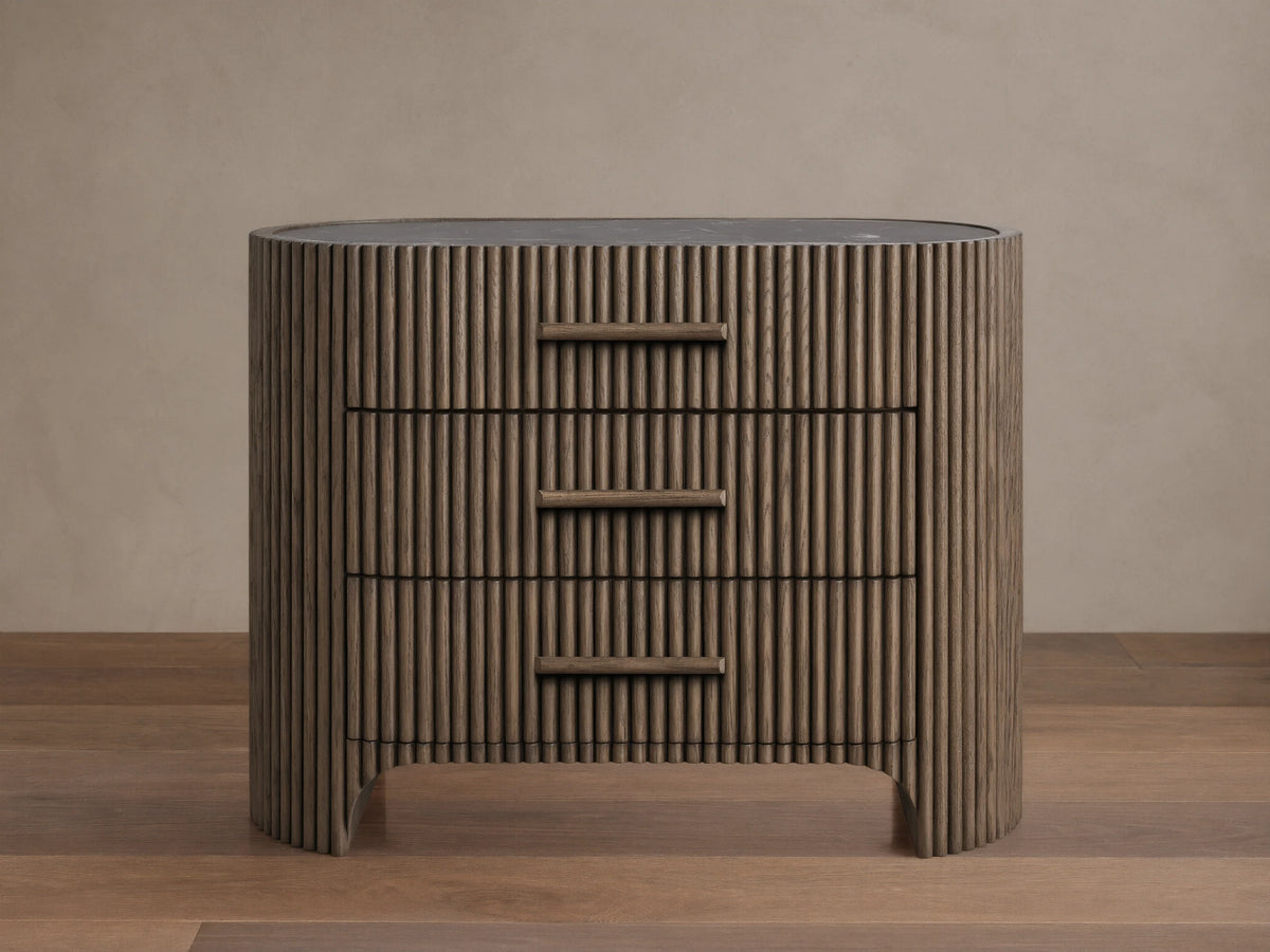 Astor Nightstand: Dark brown oak with reeding, curved sides, 3 drawers with integrated wood pulls, dark marble top.