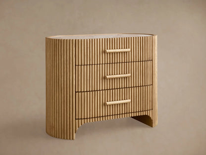 Astor Nightstand: Light oak nightstand with vertical reeding, 3 drawers, wooden pulls, and a light marble top, on a wooden floor.
