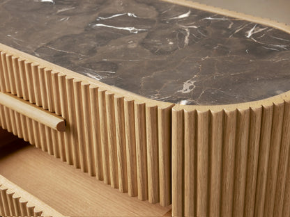 Astor Nightstand: Light oak veneer with reeded detail, oval dark marble top. Two lower drawers are open, showing wood pulls.