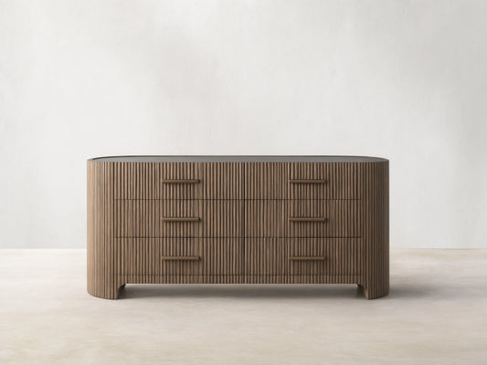 Astor Six-Drawer Dresser with oak veneer and solid oak reeding, featuring three drawers with stone pulls, set in a minimalist room.