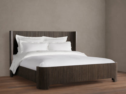 Astor Bed with solid oak reeding, dark finish. White bedding with pillows contrasts the vertical slats, set on wooden floor.