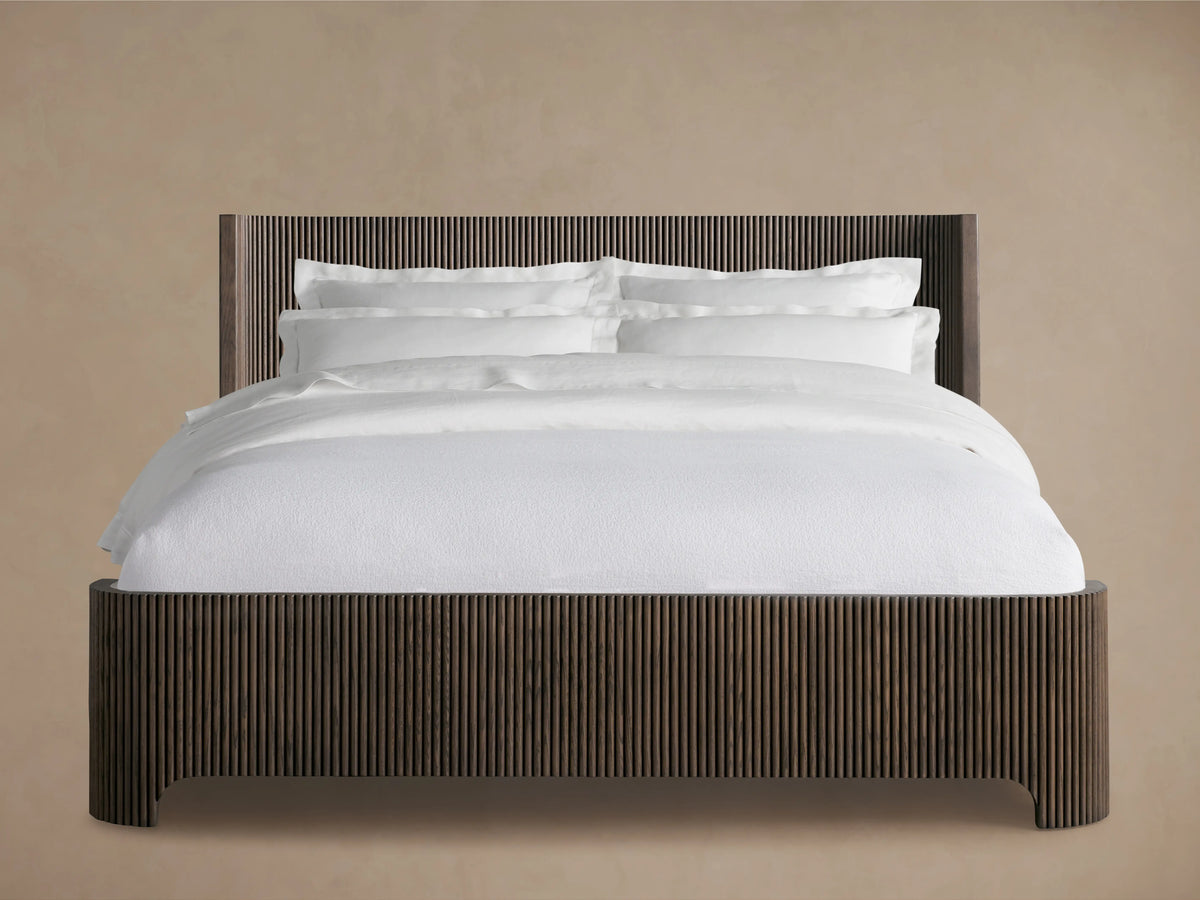Astor Bed with solid oak reeding, dark finish. White bedding with pillows contrasts the vertical slats, set on wooden floor.