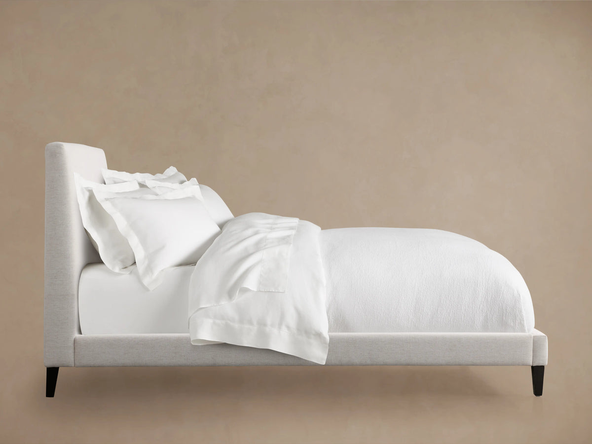 Beck Bed in side view, featuring a solid larch wood frame, white bedding, and dark catalpa wood legs against a beige background.
