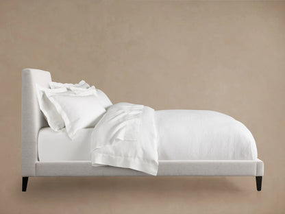 Beck Bed in side view, featuring a solid larch wood frame, white bedding, and dark catalpa wood legs against a beige background.