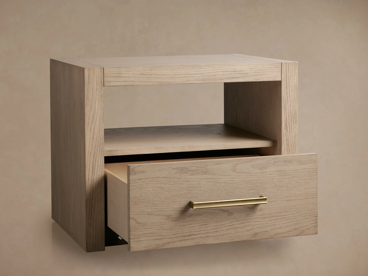 Bodhi Open Nightstand made from solid white oak with a visible wood grain. Features an open shelf and a partially open drawer with champagne brass handle.