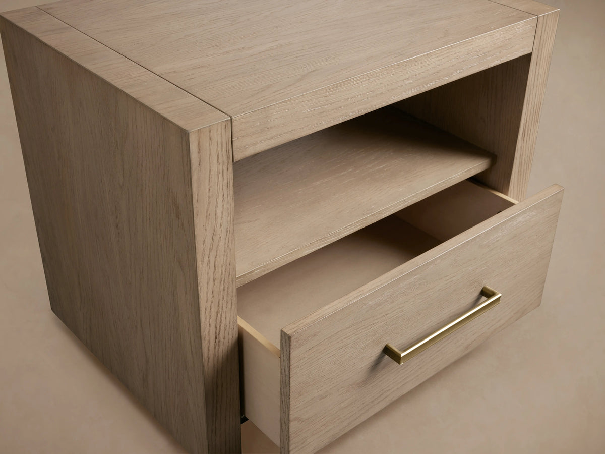 Bodhi Open Nightstand in light oak finish with an open shelf and a drawer. Features brass handle in champagne tone on the half-open drawer.