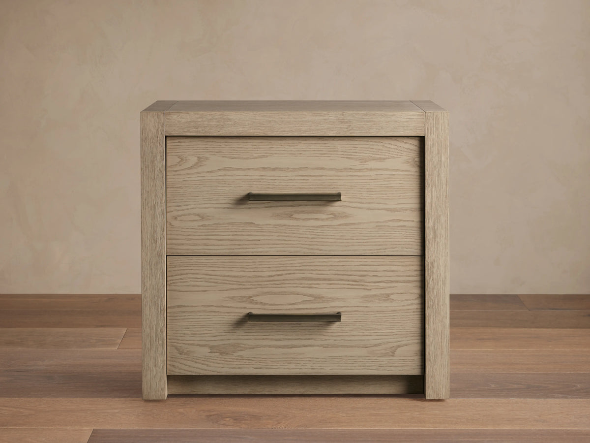 Bodhi Closed Nightstand: Light grey oak wood nightstand with two drawers and subtle champagne bar pulls, on wood floor.