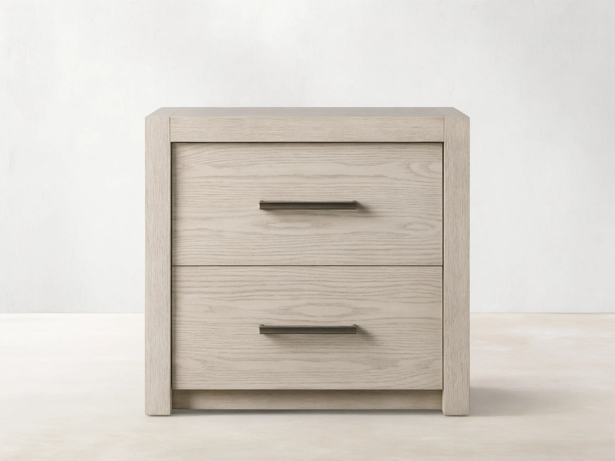 Bodhi Closed Nightstand: Light grey oak wood nightstand with two drawers and subtle champagne bar pulls, on wood floor.