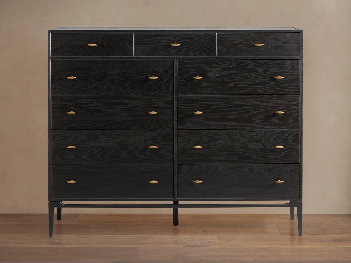 Brock Eleven-Drawer Dresser made of dark-stained ash wood with brass handles, showcasing a sleek, handcrafted silhouette on a wood floor.