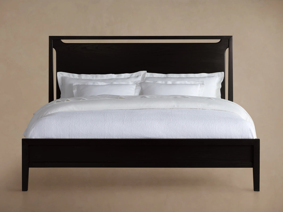 Brock Bed in rich ebony, featuring a high, solid ash wood headboard with brushed brass accents, dressed in white bedding.