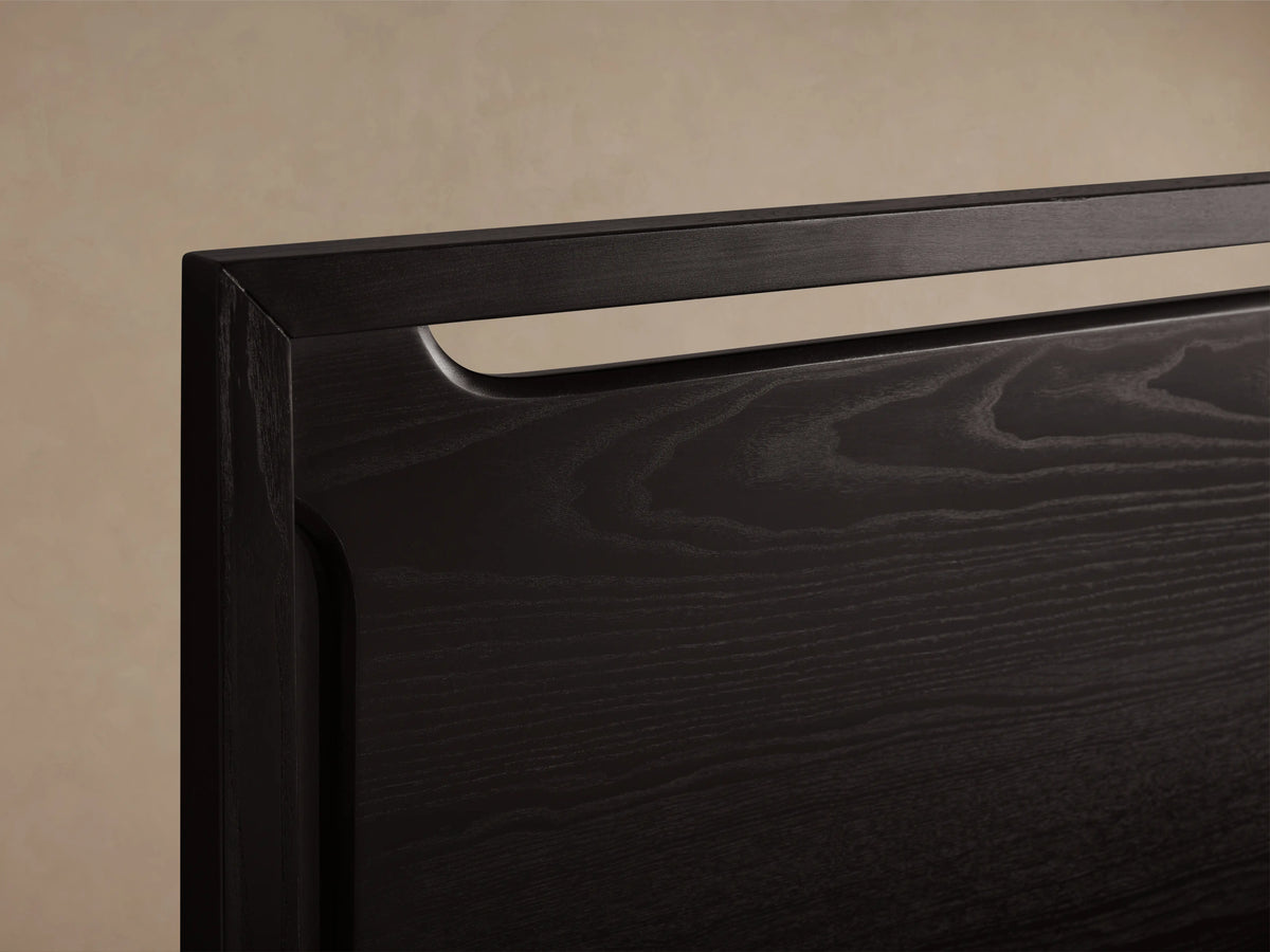 Ebony-colored Brock Bed with a high solid ash wood headboard and white bedding, set on a wooden floor in a beige room.