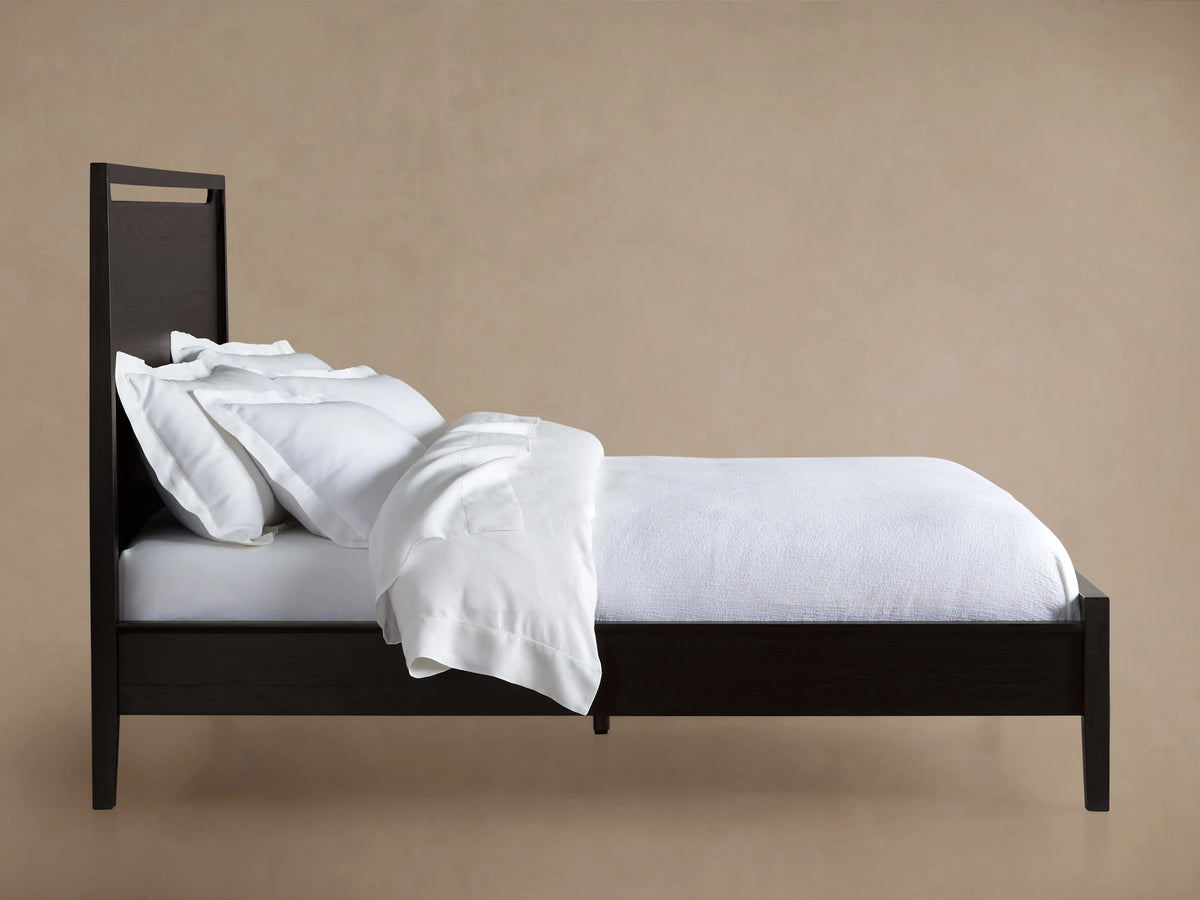 A close-up of the Brock Bed's headboard, showcasing its rich ebony-stained ash wood with visible wood grain texture.