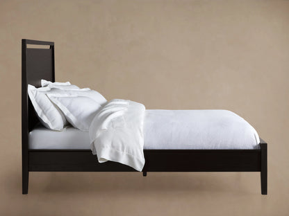 A close-up of the Brock Bed's headboard, showcasing its rich ebony-stained ash wood with visible wood grain texture.