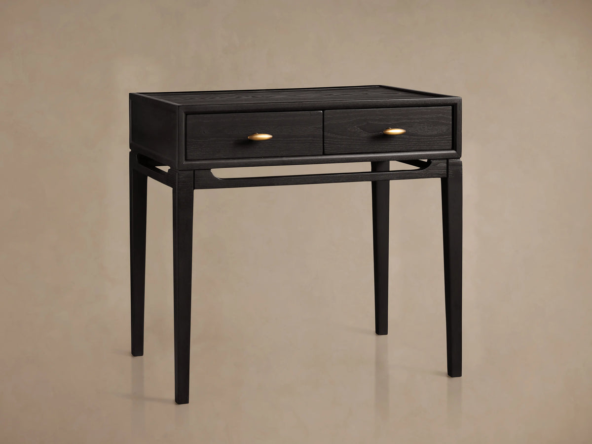 Brock Nightstand in ebony-stained ash wood with two drawers, brass hardware, and tapered legs, set against a beige background.