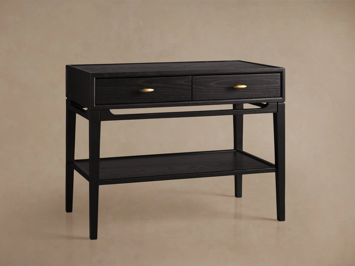 Brock Nightstand in rich ebony with two front drawers featuring brushed brass handles, additional lower shelf, on a beige background.