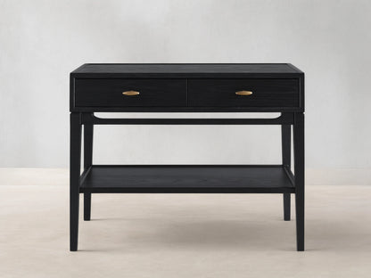 Brock Nightstand in ebony ash wood with two brass-handled drawers and lower shelf, set on flat wood flooring against beige wall.
