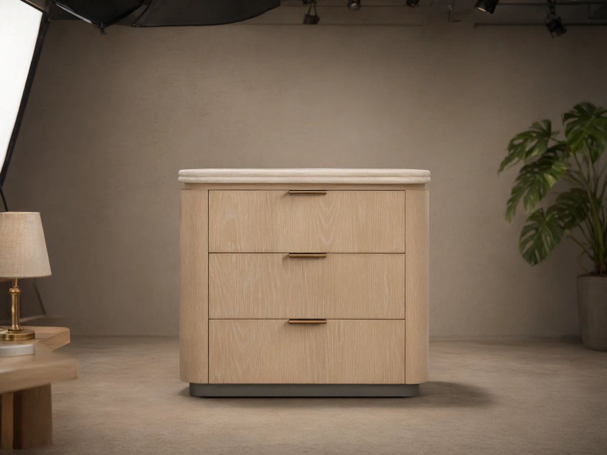 Caden Nightstand, sand finish oak veneer, light stone top, 3 drawers with pewter edge-pulls, on wood floor.