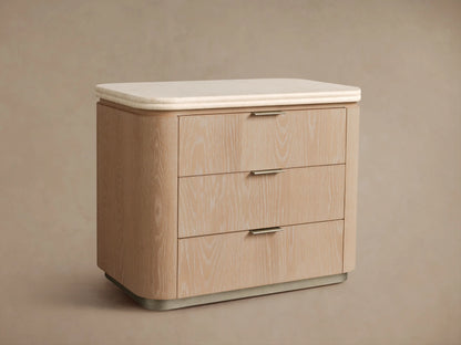 Caden Nightstand, sand finish oak veneer, light stone top, 3 drawers with pewter edge-pulls, on wood floor.