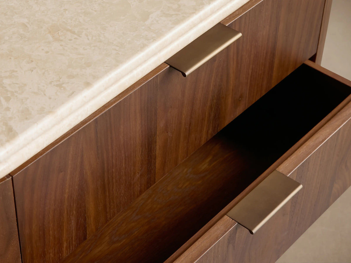 Caden Nightstand: dark walnut wood with rounded corners, light stone top, and three drawers with antique bronze pulls.