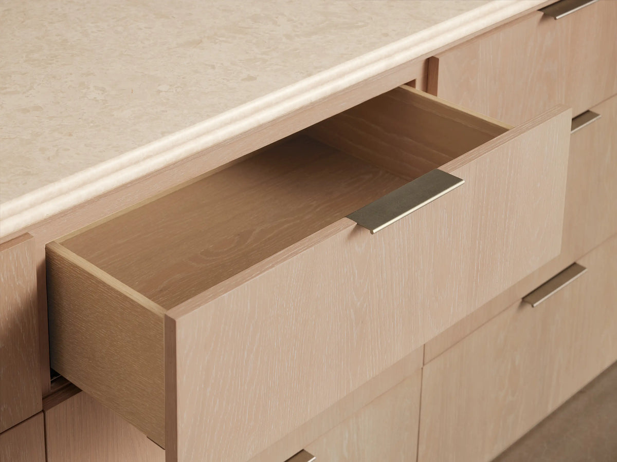 Caden Nine-Drawer Dresser: light sand oak veneer with rounded edges, a light stone top, and pewter hardware.