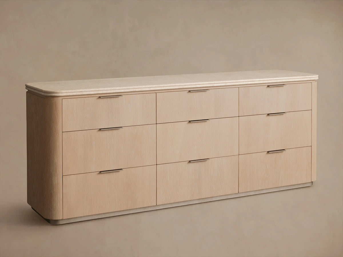 Caden Nine-Drawer Dresser, sand oak veneer with light speckled stone top. One drawer is open, revealing light wood interior and pewter edge-pull handle.