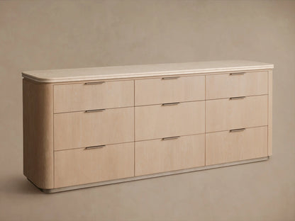 Caden Nine-Drawer Dresser, sand oak veneer with light speckled stone top. One drawer is open, revealing light wood interior and pewter edge-pull handle.