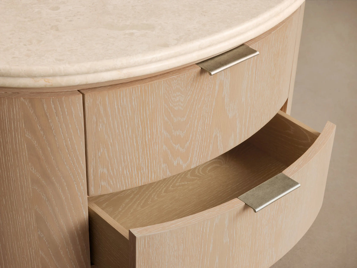 Caden Oval Nightstand in light sand oak veneer with visible grain, two drawers with pewter pulls, and a cream stone top.