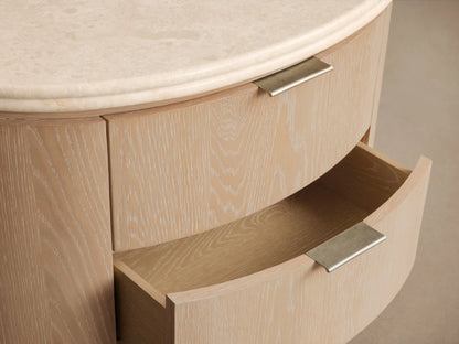 Caden Oval Nightstand in light sand oak veneer with visible grain, two drawers with pewter pulls, and a cream stone top.