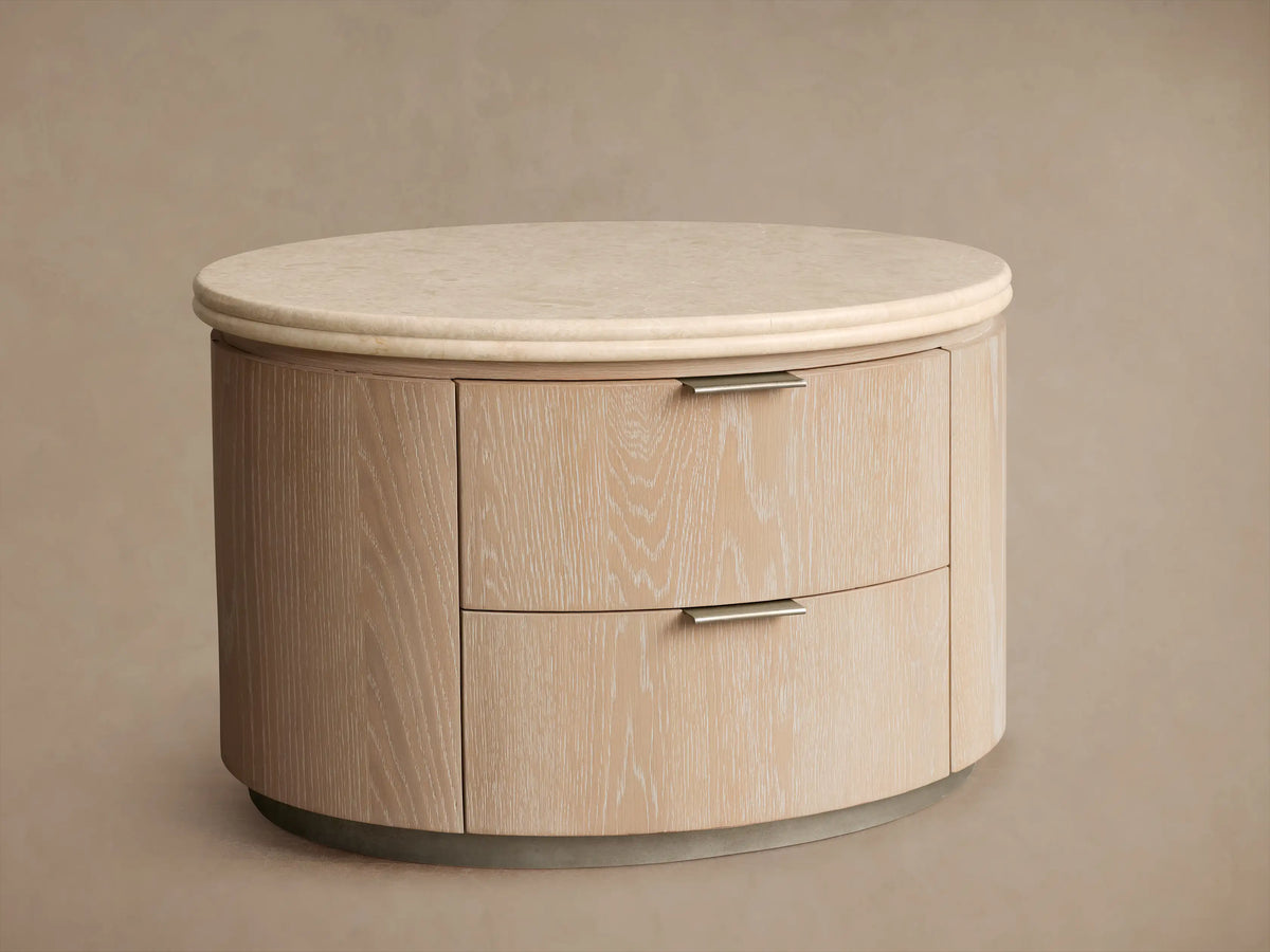 Close-up of Caden Oval Nightstand. Light sand oak veneer body, light stone top, pewter edge pulls. Second drawer open.