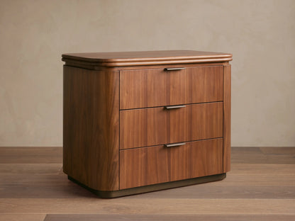 Front view of Caden Wood Nightstand. Walnut veneer with subtle sheen, rounded top, 3 drawers with antique bronze edge pulls.