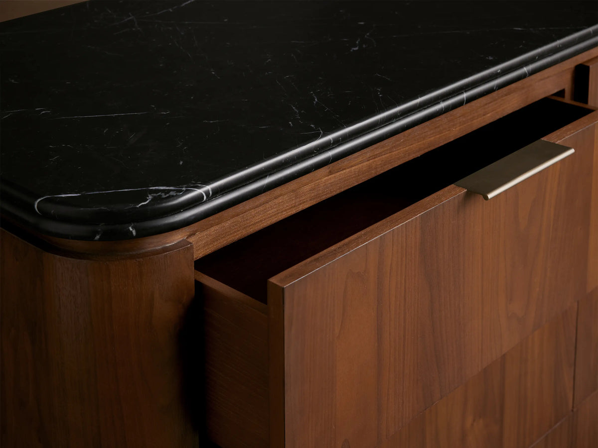 Caden Nine-Drawer Dresser, light walnut wood with rounded edges, dark stone top, and antique bronze pulls, on a wood floor.