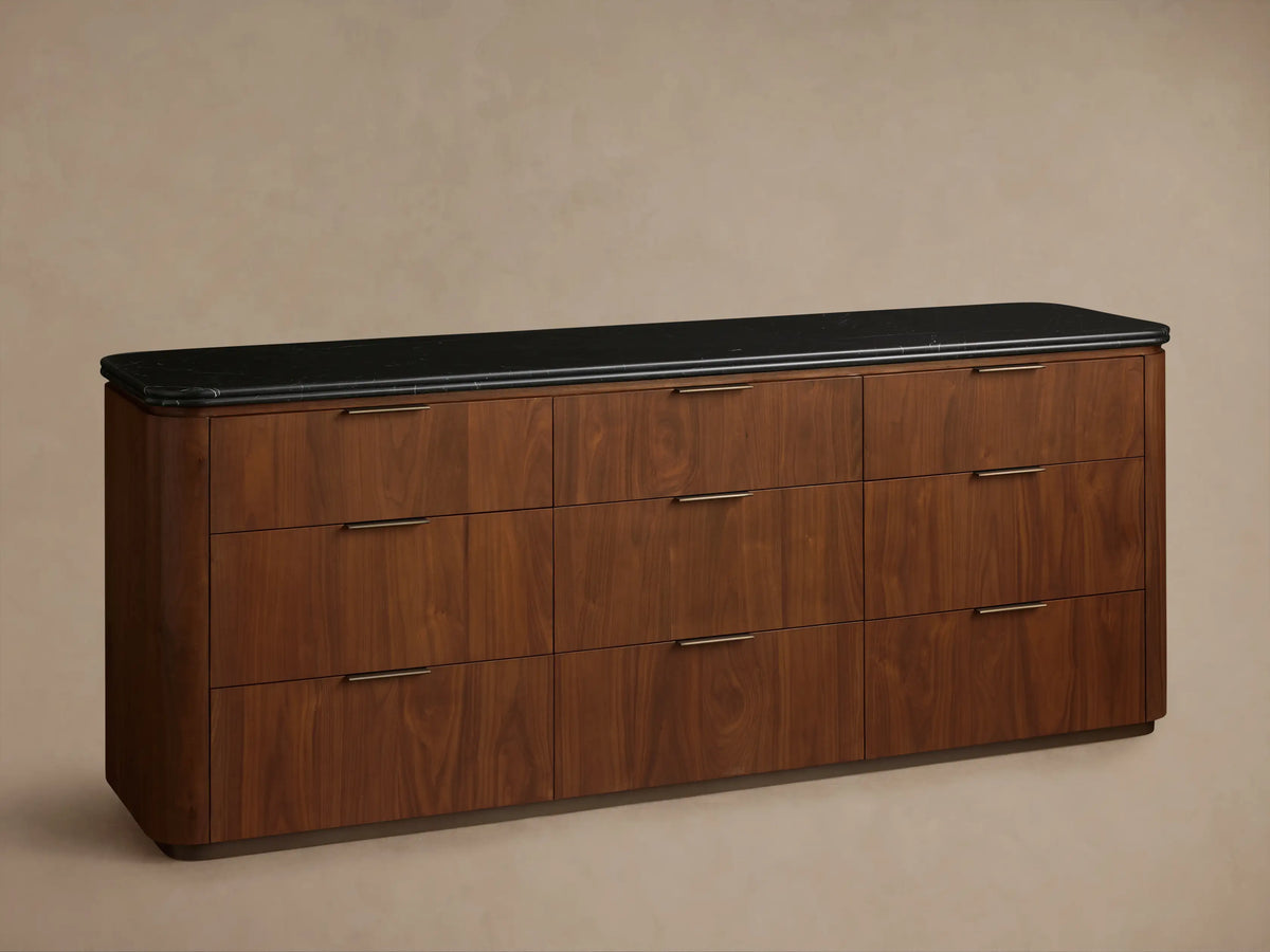Close-up of Caden Nine-Drawer Dresser. Dark brown walnut wood, black marble top with rounded edge, open drawer with bronze pull.