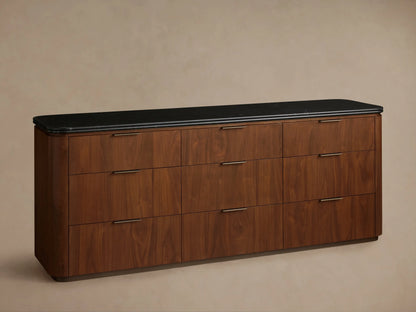 Close-up of Caden Nine-Drawer Dresser. Dark brown walnut wood, black marble top with rounded edge, open drawer with bronze pull.