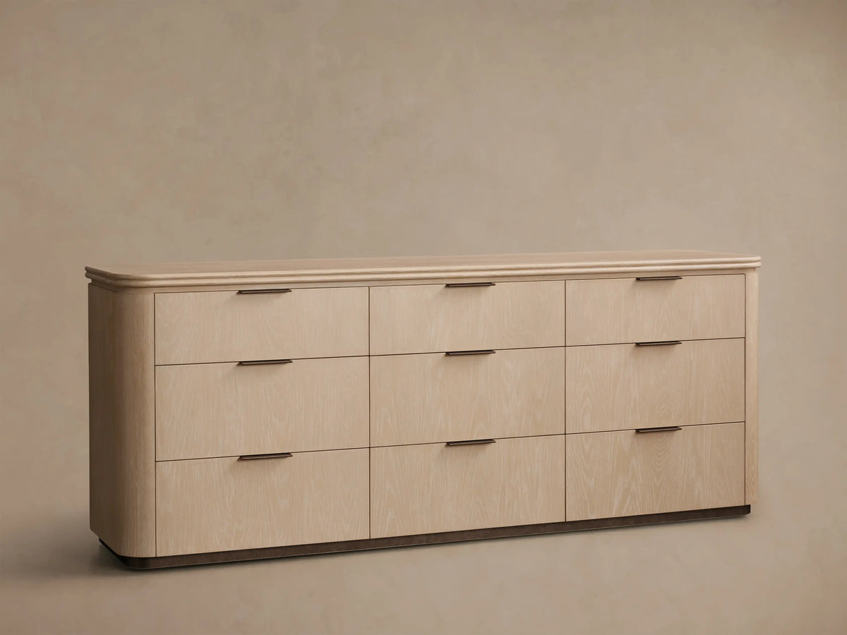 Front view of Light walnut Caden Wood Nine-Drawer Dresser with antique bronze edge-pull hardware and rounded top.