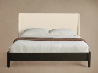 Calista Bed with cream upholstered headboard, dark brown wood frame, white textured bedding, and a brown throw.