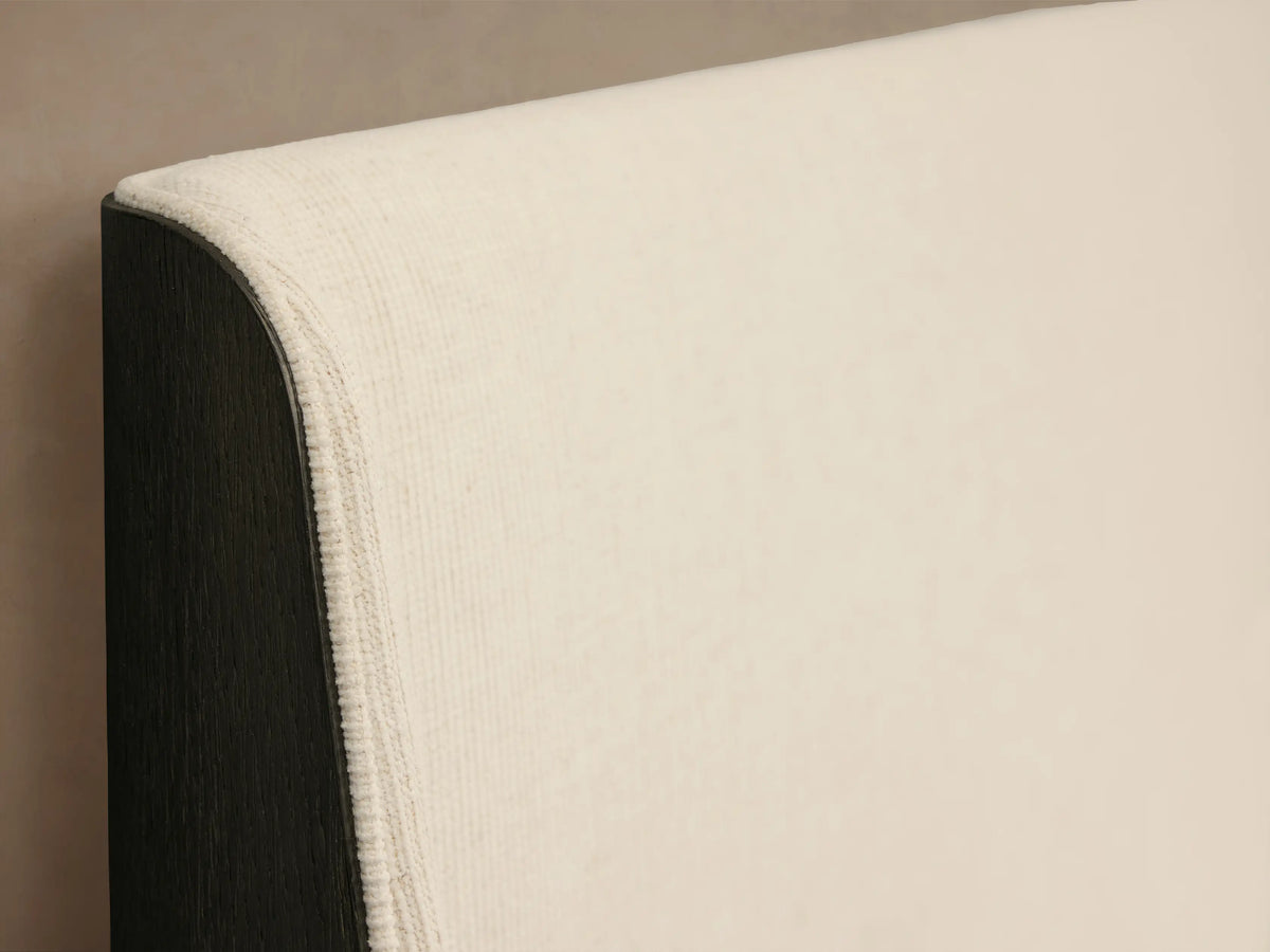 Calista Bed with dark wood frame, light cream upholstered headboard, cream bedding, and a brown throw blanket, front view.